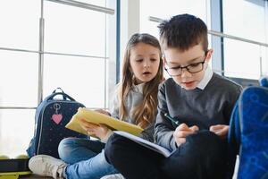 retrato de sonriente colegio niños en colegio corredor con libros foto