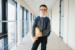 Portrait of happy school student. Smart elementary school kid glasses standing in school. Little child in holding a book photo