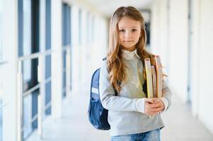 Front view of pretty blonde school girl holding many colorful notes and books. Clever teen girl smiling at camera, standing on corridor of international school photo