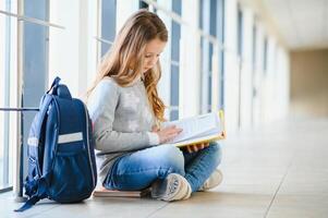 Front view of pretty blonde school girl holding many colorful notes and books. Clever teen girl smiling at camera, standing on corridor of international school. photo