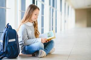 Front view of pretty blonde school girl holding many colorful notes and books. Clever teen girl smiling at camera, standing on corridor of international school photo