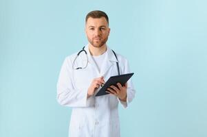 Medic in white robe, looking straight at camera with positive smile, holding tablet computer next to chest while working in hospital, isolated on blue background photo