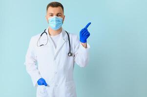 Male doctor, in a white coat and gloves, points to the side with his hands. next to the text space. blank on a blue background photo