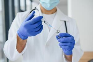 Doctor in PPE holding a vial or bottle vaccine against coronavirus Covid 19 new Omicron variant or strain in his hand, close up. Concept of vaccination, trial and treatment due to SARS-CoV-2 pandemic. photo