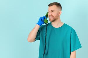 Portrait of young male doctor with phone, on blue background photo