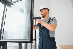 Construction worker using drill while installing window indoors photo