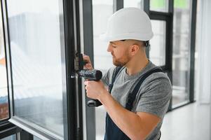 Construction worker using drill while installing window indoors photo