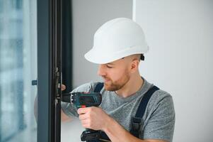 Workman in overalls installing or adjusting plastic windows in the living room at home photo