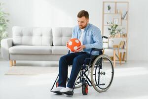 Disabled man in wheelchair holding ball with sadness, cannot play game, feeling depressed at home. photo