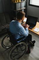 Young man with special needs in casual clothes working on wireless laptop. Male freelancer working from home while sitting in wheelchair photo