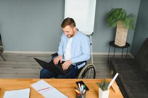 Young happy entrepreneur in wheelchair working on laptop at home. photo