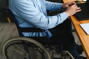 Young happy entrepreneur in wheelchair working on laptop at home photo