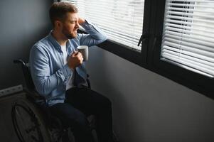 Young disabled man sitting in a wheelchair near the window photo