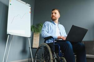 discapacitado empresario sentado en silla de ruedas utilizando computadora a lugar de trabajo foto