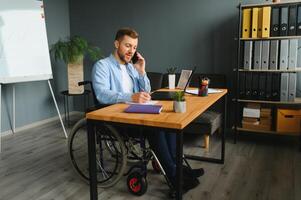 Young happy entrepreneur in wheelchair working on laptop at home photo