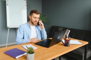 Young man with special needs in casual clothes working on wireless laptop. Male freelancer working from home while sitting in wheelchair. photo