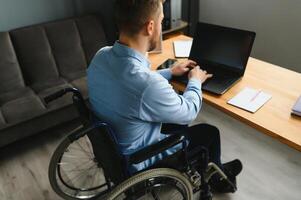 Young happy entrepreneur in wheelchair working on laptop at home. photo