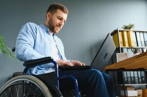 discapacitado persona en el silla de ruedas trabajos en el oficina a el computadora. él es sonriente y apasionado acerca de el flujo de trabajo foto