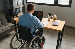 Disabled person in the wheelchair works in the office at the computer. He is smiling and passionate about the workflow. photo