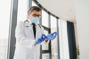 male doctor in a protective mask puts on gloves in the clinic photo