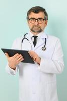 Senior doctor man wearing stethoscope and medical coat oveer blue background photo