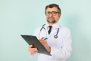 Senior doctor man wearing stethoscope and medical coat over blue background. Cheerful expression photo