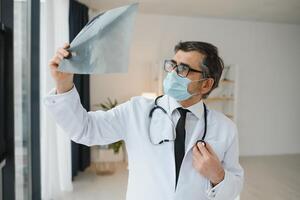 un mayor médico mirando a el radiografía en su oficina. foto