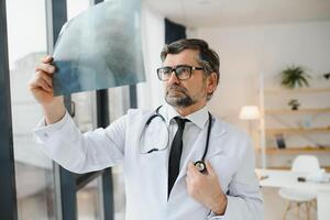 un mayor médico mirando a el radiografía en su oficina. foto