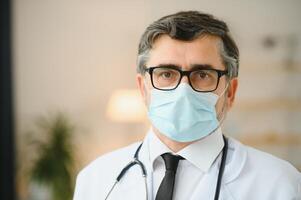 Mature old medical healthcare professional doctor wearing white coat, stethoscope, glasses and face mask. Medical staff health care protection concept. Portrait. photo