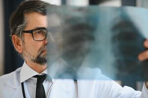 older man doctor examines x-ray image of lungs in a clinic photo