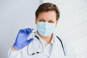 Closeup hand of woman doctor or scientist in doctor's uniform wearing face mask protective in lab holding medicine liquid vaccines vial bottle, coronavirus or COVID-19 concept photo