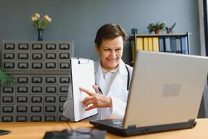 Portrait of female doctor counseling patient via video call. Professional physician in white lab coat gesturing and explaining course of treatment sitting at office desk during online consultation. photo