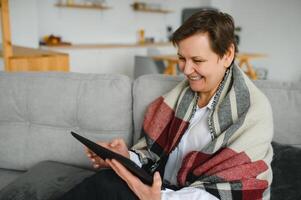 Middle-aged woman reading a message, e-book or information on her tablet computer with a look of excited anticipation as she sits on a couch at home photo