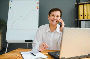 Elderly woman working on laptop computer, talking on the phone. photo