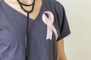 Shot of the female doctor against the white wall with pink ribbon, as a symbol of a breast cancer awareness. Concept photo