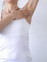 Shot of the woman in the white top against the white wall, performing self examination of the breasts, looking for abnormalities. Cancer awareness photo