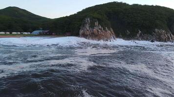 Aerial view of large storm waves rolling onto a rocky shore at dawn video