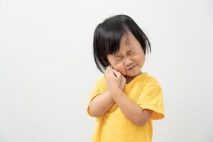 little asian girl presses hand to cheek, suffers from pain in tooth. Teeth decay, dental problems, child emotions and facial expression, oral health care, reducing sweets, fluorine coating photo