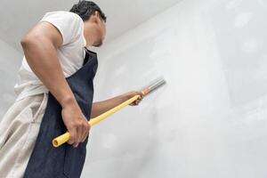 painter man, brush in hand for products to restore and paint the wall, indoor the building site of a house, wall during painting, renovation, painting, contractor, Architect, construction worker photo