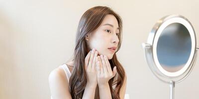 Beautiful Asian woman sit in front of a mirror. face of a healthy woman applying cream and makeup. Advertisement for skin cream, anti-wrinkle, baby face, whitening, moisturizer, tighten pores serum photo