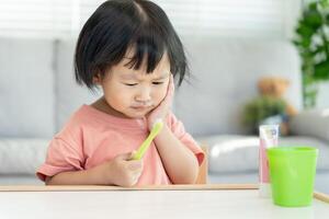 little asian girl presses hand to cheek, suffers from pain in tooth. Teeth decay, dental problems, child emotions and facial expression, oral health care, reducing sweets, fluorine coating photo