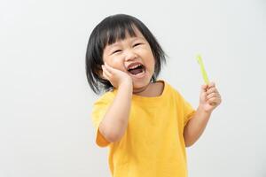 pequeño asiático niña prensas mano a mejilla, sufre desde dolor en diente. dientes decadencia, dental problemas, niño emociones y facial expresión, oral salud cuidado, reduciendo dulces, flúor revestimiento foto