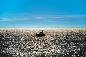 Fisherman on a boat in backlight in the middle of the sea photo