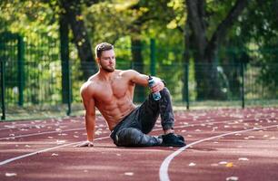 Shirtless Man Resting on Running Track photo