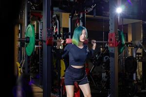 Asian muscular sport woman is practice weight training on deadlift barbell for core muscle inside gym with dark background for exercising and workout concept photo