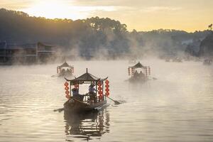 Chinese style tourist boat attraction at Ban Rak Thai village, Mae Hong Son, Thailand during winter morning sunrise with misty fog over the lake for travel destination and tourism concept photo