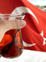 A cup of tea in a woman's hand against the background of the Turkish flag, Bosphorus and Istanbul photo