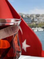 A cup of tea in a woman's hand against the background of the Turkish flag, Bosphorus and Istanbul photo