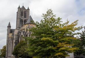 otoño ver de Santo nicolás Iglesia en Gante enmarcado por un vibrante árbol con dorado hojas foto