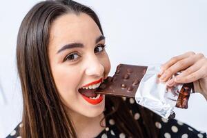 mujer disfrutando un mordedura de delicioso chocolate. un mujer mordiendo dentro un bar de chocolate foto
